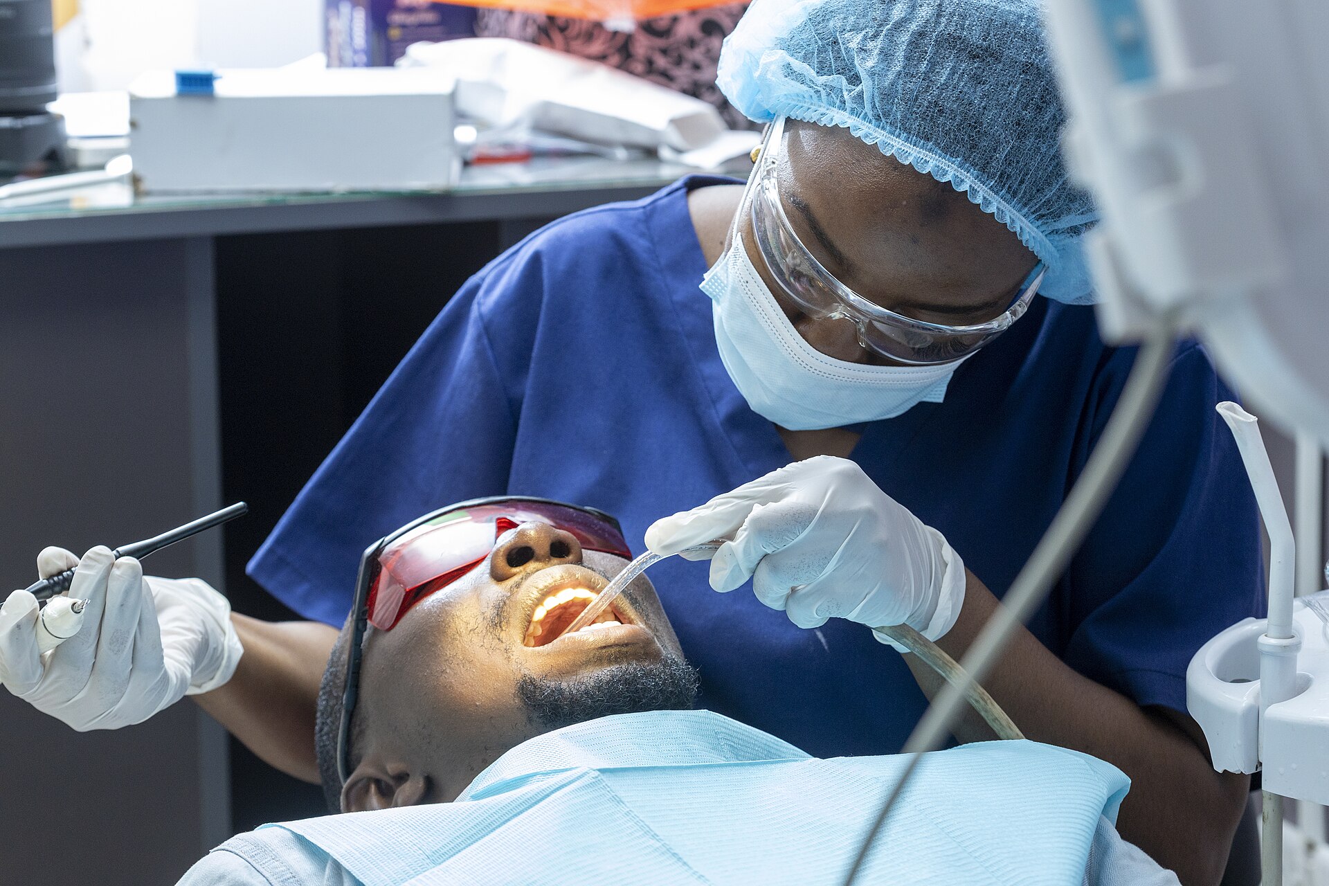 Dentist in mask and cap treating a patient who wears protective glasses